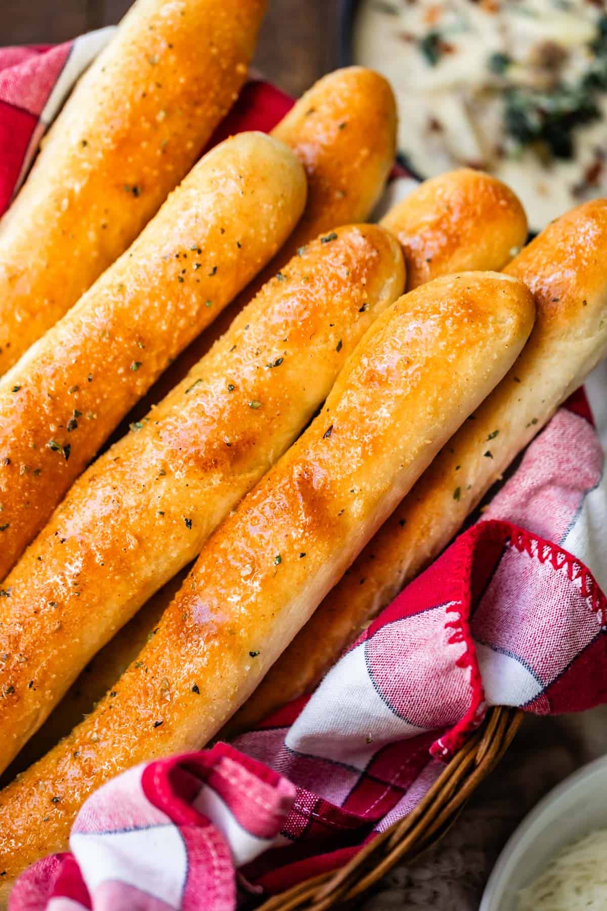 A basket filled with golden-brown breadsticks topped with herbs.