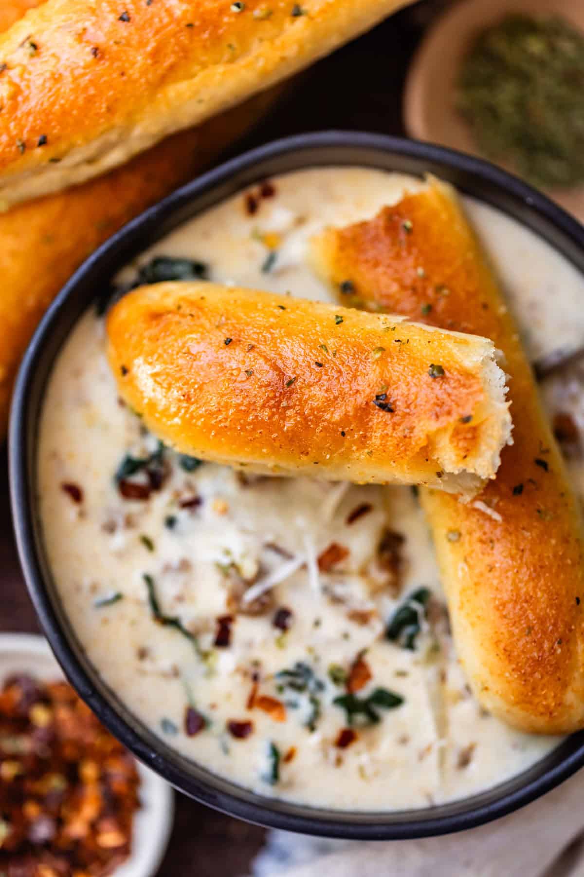 A black bowl of creamy soup with sausage and greens, topped with two pieces of golden-brown garlic bread.