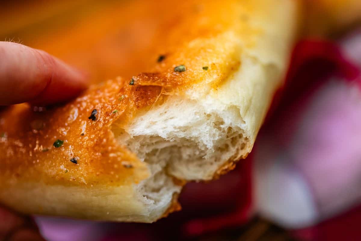 A hand holding a piece of golden-brown focaccia bread with a torn, soft interior.