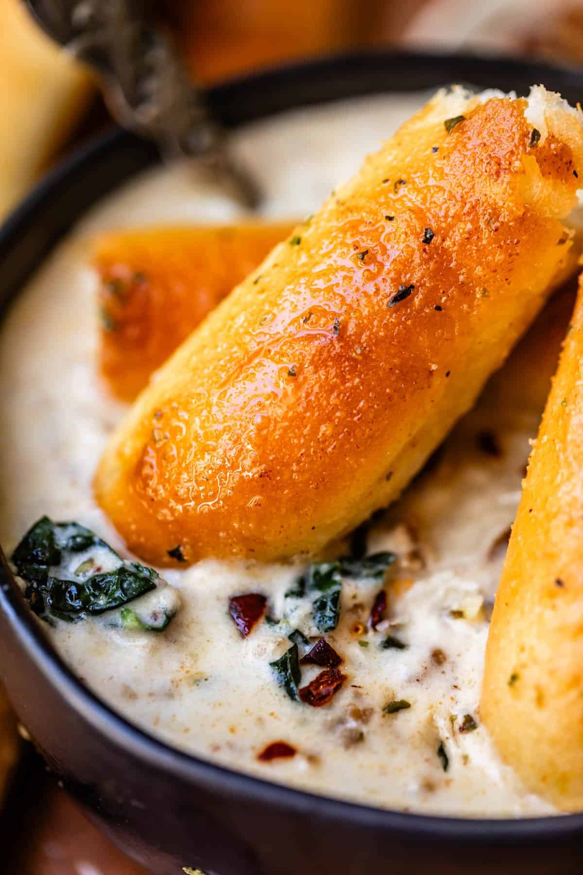 Two garlic breadsticks resting in a creamy soup with spinach and red pepper flakes.