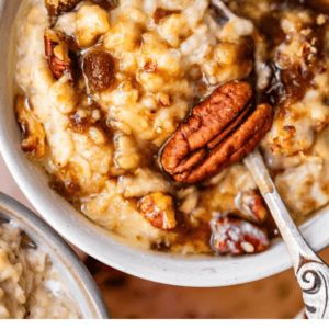 A bowl of oatmeal topped with butterscotch sauce and pecans, with a spoon resting inside.