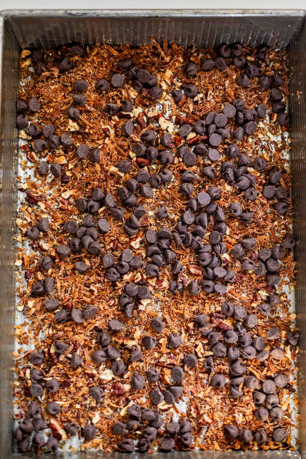 A baking sheet filled with a mixture of chopped nuts, toasted coconut, and dark chocolate chips.