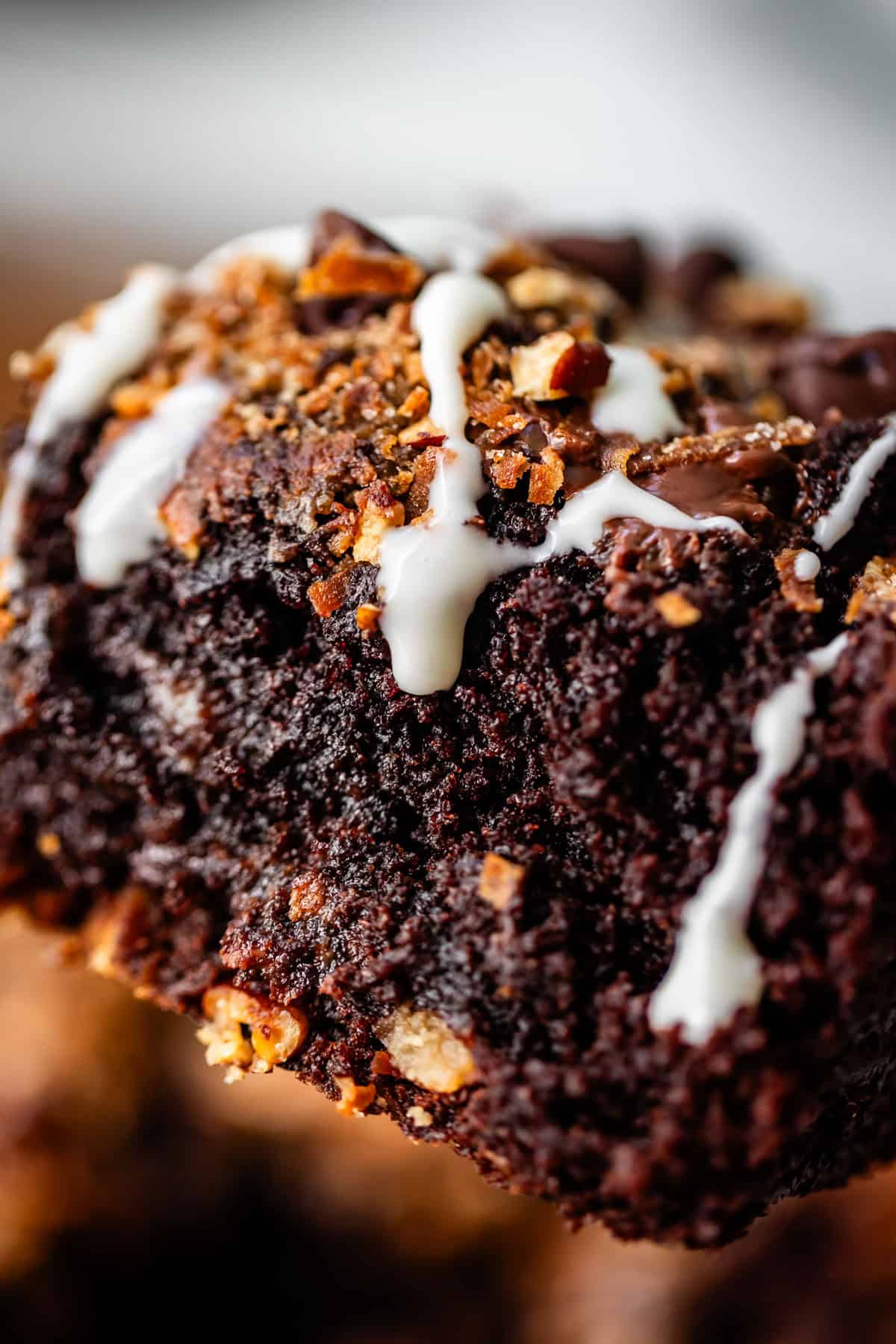 A close-up of a chocolate brownie drizzled with white icing and topped with bits of bacon.