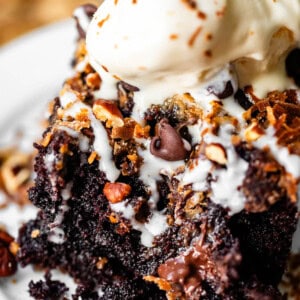 A slice of chocolate cake topped with a scoop of melting vanilla ice cream, chocolate chips, and nuts.