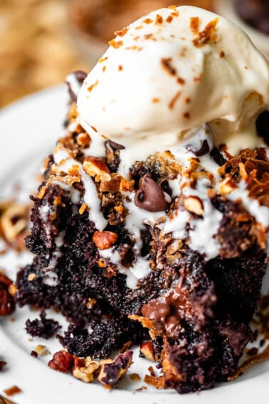 A slice of chocolate cake topped with a scoop of melting vanilla ice cream, chocolate chips, and nuts.